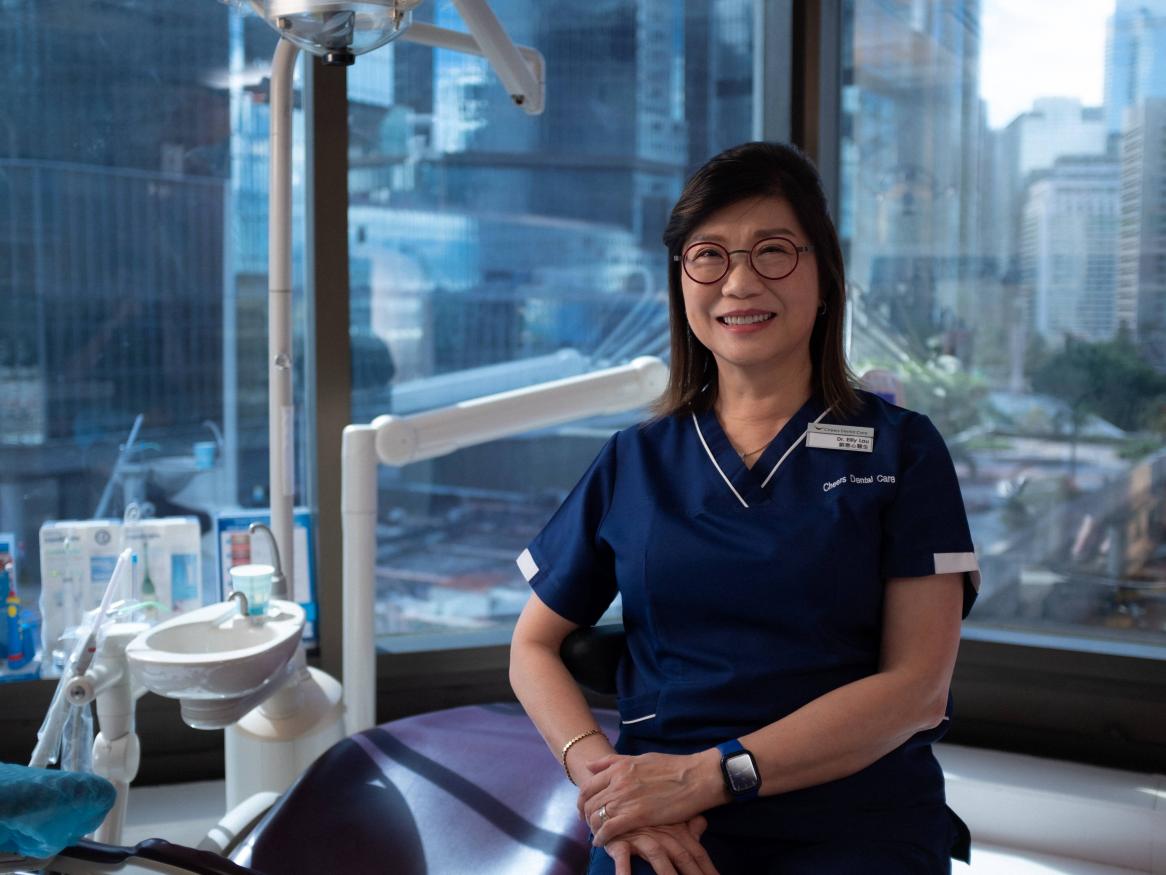 A portrait of Eilly in scrubs in her dental surgery, Hong Kong in the background