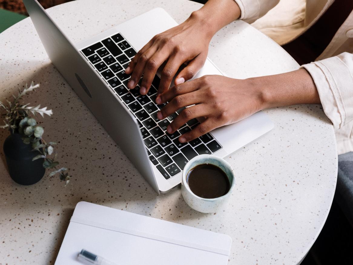 Woman typing at a laptop with a cup of coffee