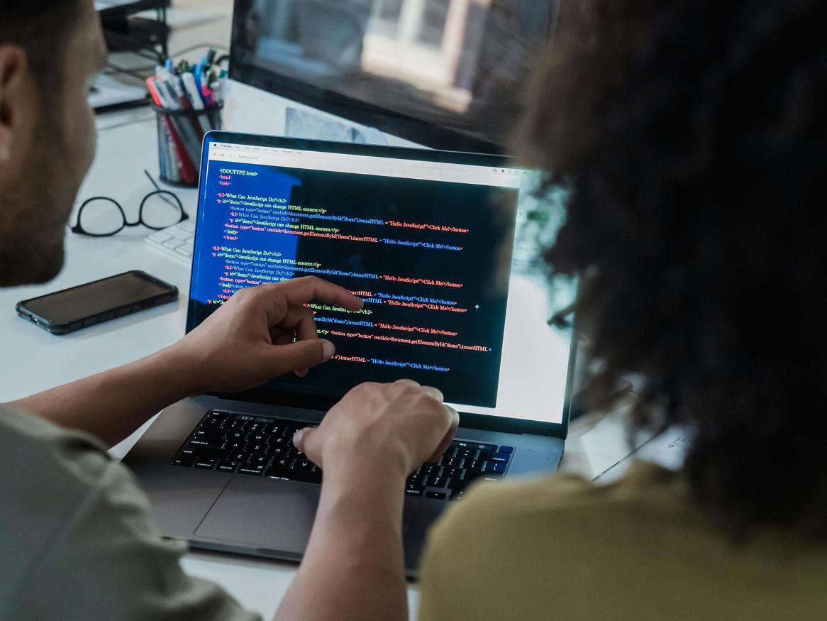 Two people reading HTML code on a laptop screen